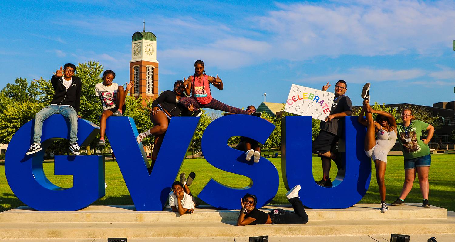 A group of students pose around the GVSU letter sculpture on GVSU's Allendale campus.